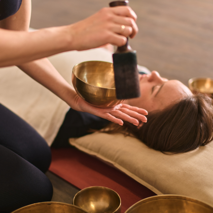 Practitioner playing a singing bowl beside a client during a private one-to-one sound bath session promoting deep relaxation and wellbeing.